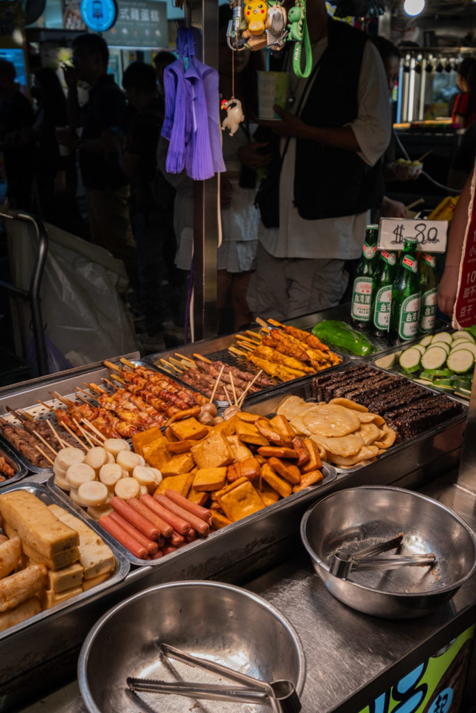 Raohe night market street food stalls with tofu and skewers