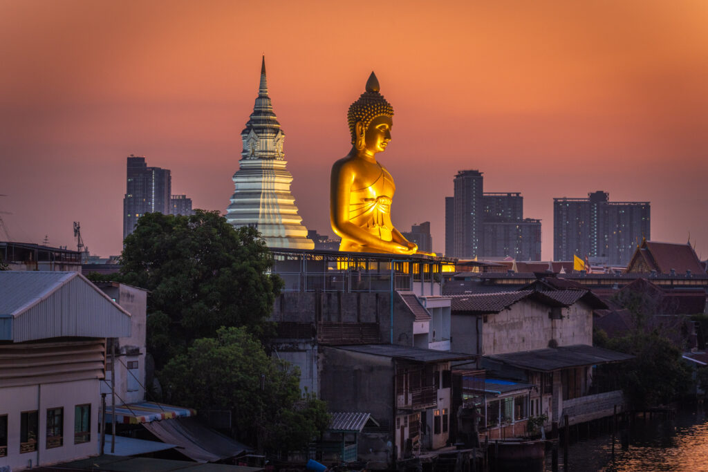 Wat Paknam Phasi Charoen golden buddha as seen from overpass during blue hour with orange sky.