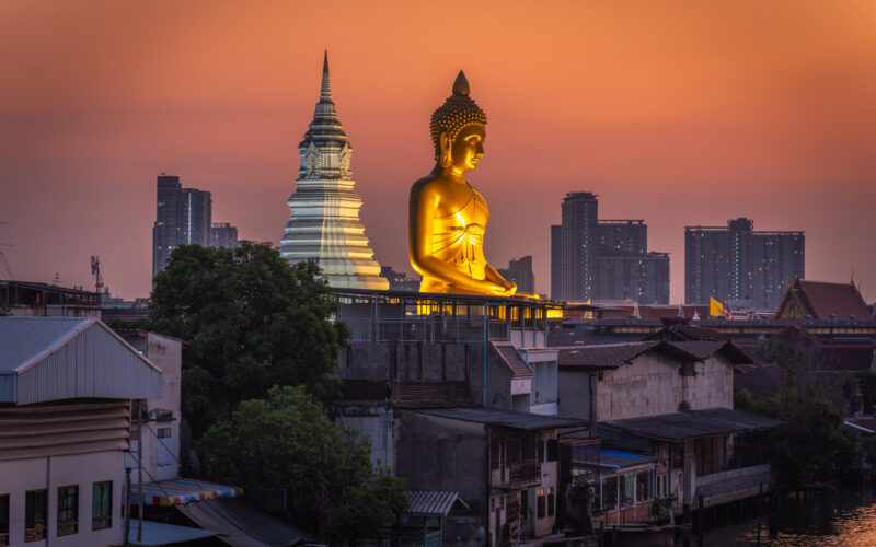 Wat Paknam Phasi Charoen golden buddha as seen from overpass during blue hour with orange sky.